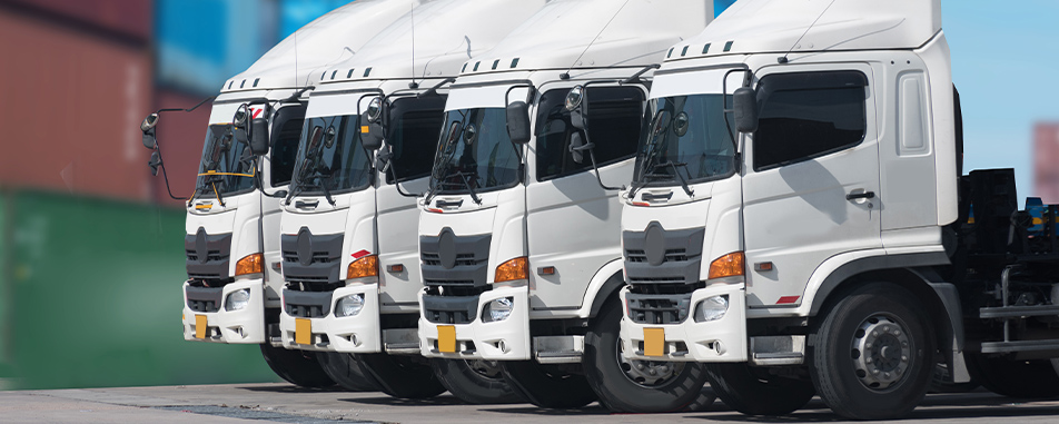 Five white cargo trucks lined up side by side in a yard - flatheadinsurance.com