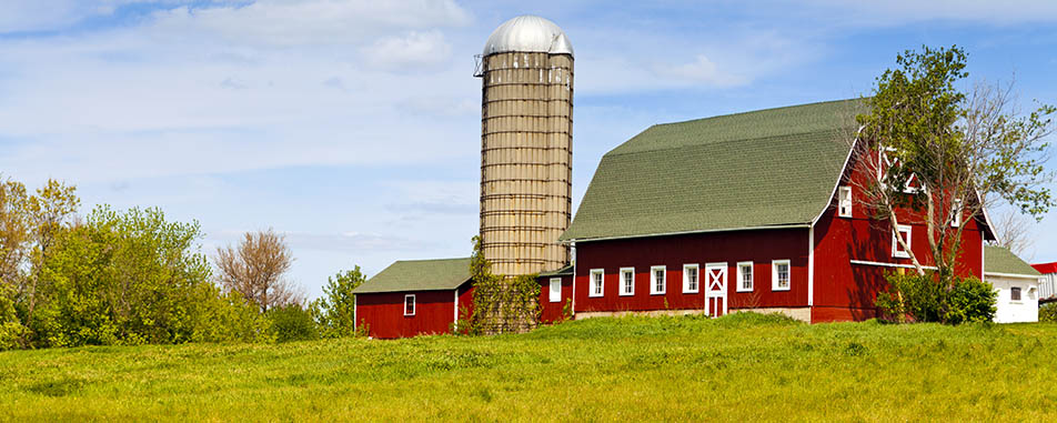Red barn with green roof and large silo set amid lush greenery under a partly cloudy sky - flatheadinsurance.com