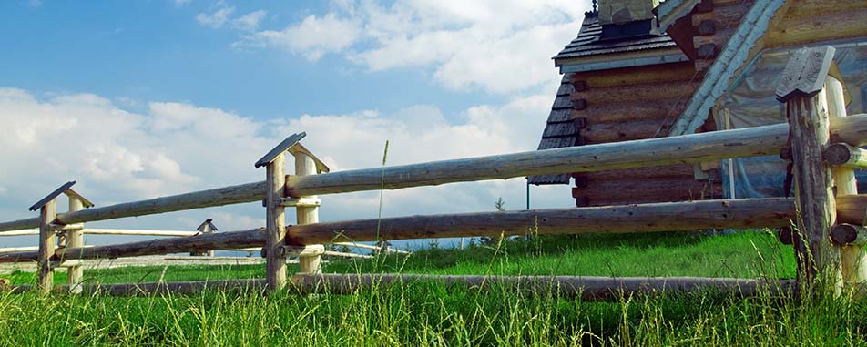 A wooden fence borders a lush green meadow under a blue sky with clouds - flatheadinsurance.com